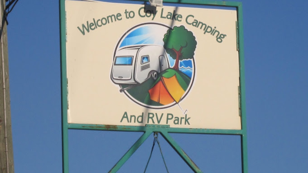 Coy Lake Camping sign featuring their logo, which is a graphic of an RV, a tree and an orange tent