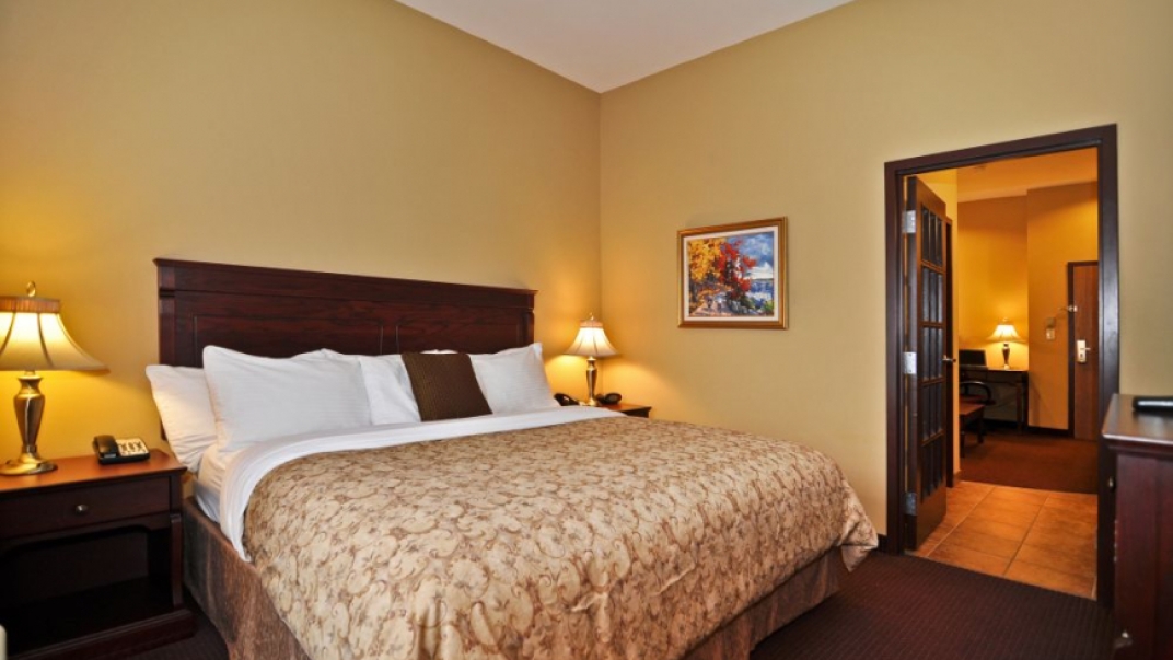 Interior shot of a hotel room with a king bed. Beige walls and dark trim.