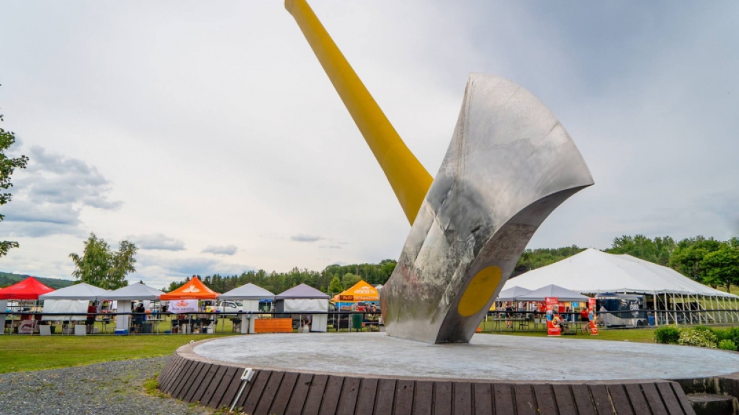 A giant axe in the ground in front of tents at the Big Axe craft Beer festival