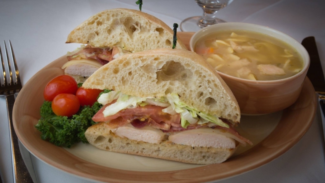 a club sandwich with soup on a pink and beige plate
