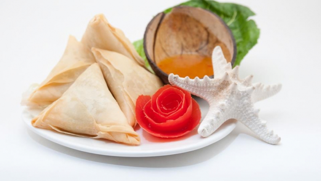 A plate with triangle pastries, a red flower, a white starfish, and half a coconut.