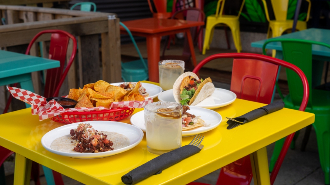 A yellow table with a red chair. There are tacos on plates on the table and a bowl of chips.