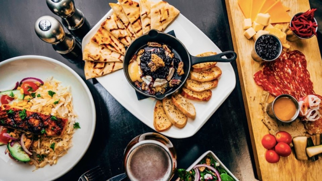 A top down view of a table with various plates of finger foods, including a cheese board and breads with dip.