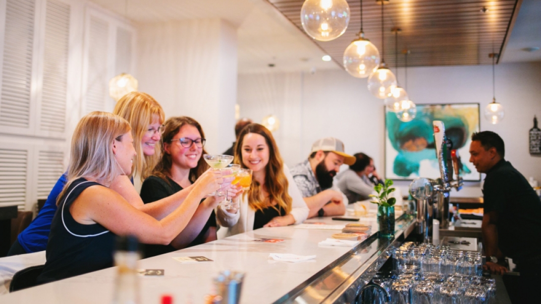group of women toasting at a white bar with a male bartender