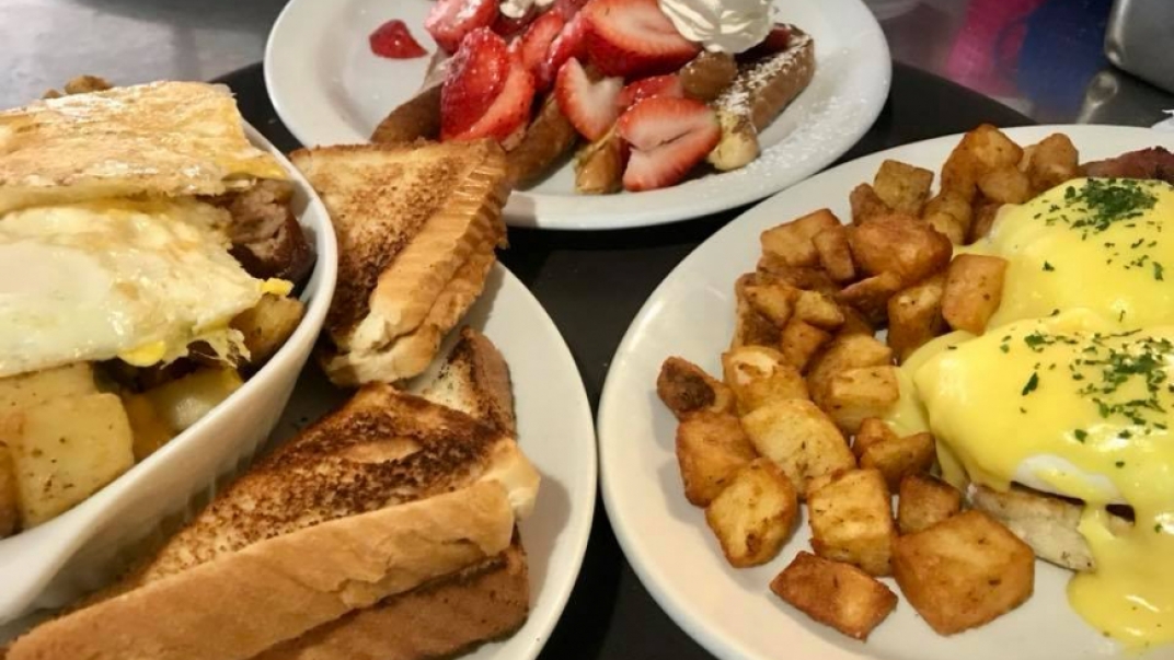 Eggs, toast, hashbrowns, strawberries and other breakfast foods on plates on a table