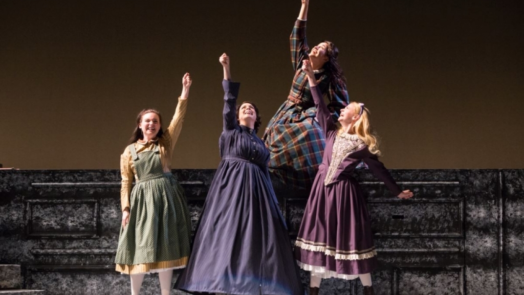 four women in period clothing raise their fist on a theatre stage