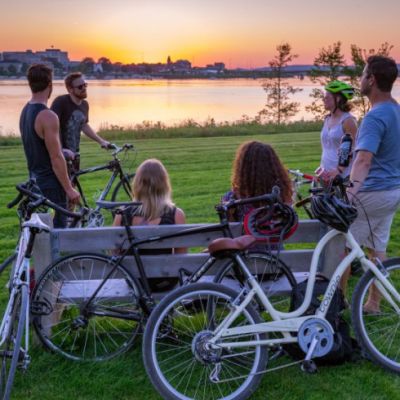 Group of people with bikes sitting on a park bench overlooking the water and city skyline