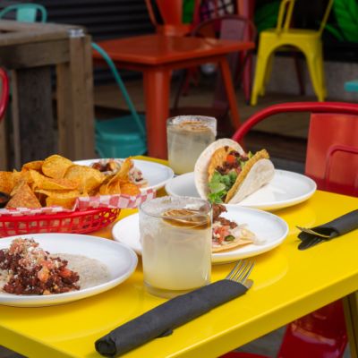 A yellow table with a red chair. There are tacos on plates on the table and a bowl of chips.