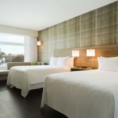 Inside shot of a hotel room with clean white sheets, pillows, and a large window.