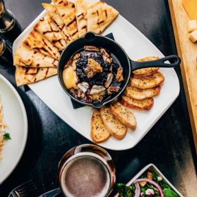 A top down view of a table with various plates of finger foods, including a cheese board and breads with dip.