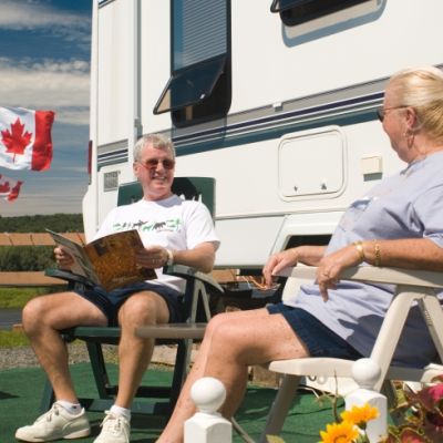 Smiling elderly couple sits on lawn chairs in front of an RV. 