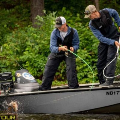 two men on a boat with fishing gear wrangling a fish to net