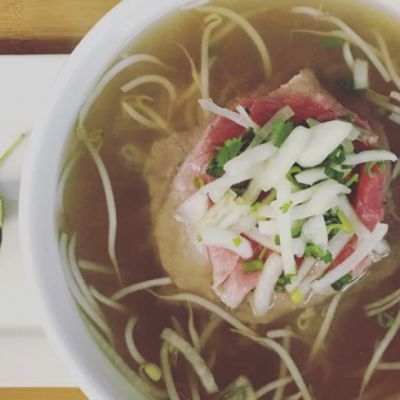 White bowl of noodle and meat in broth on a table