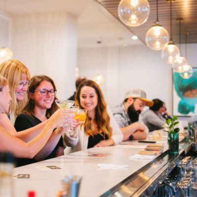 group of women toasting at a white bar with a male bartender