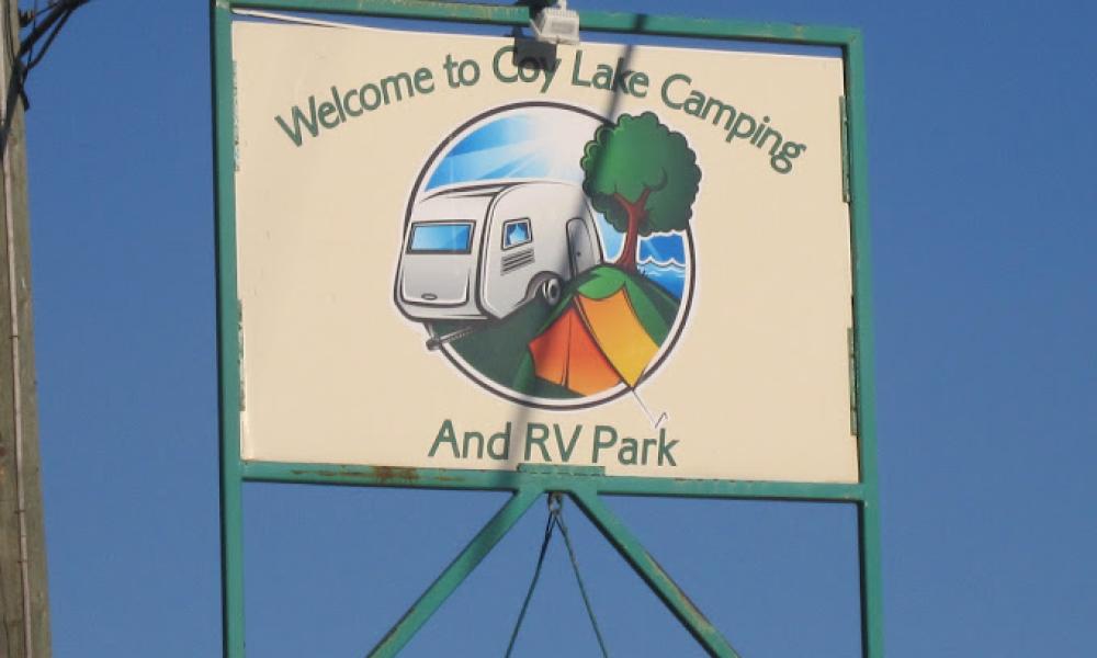 Coy Lake Camping sign featuring their logo, which is a graphic of an RV, a tree and an orange tent