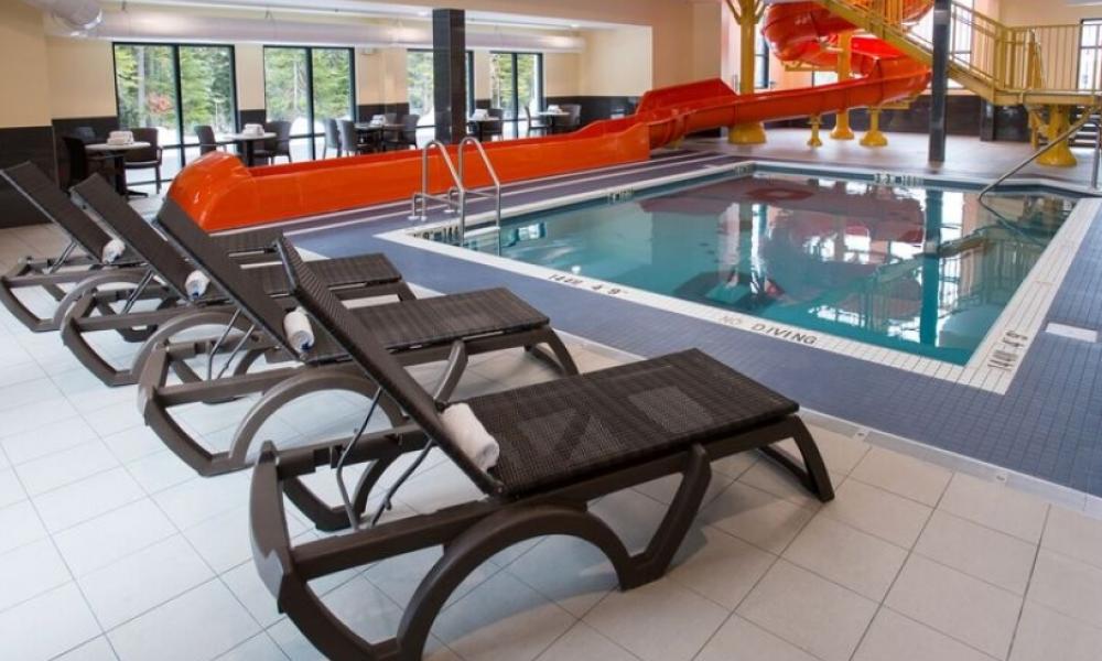 Image of an indoor pool with a red waterslide and lounge chairs on the pool deck