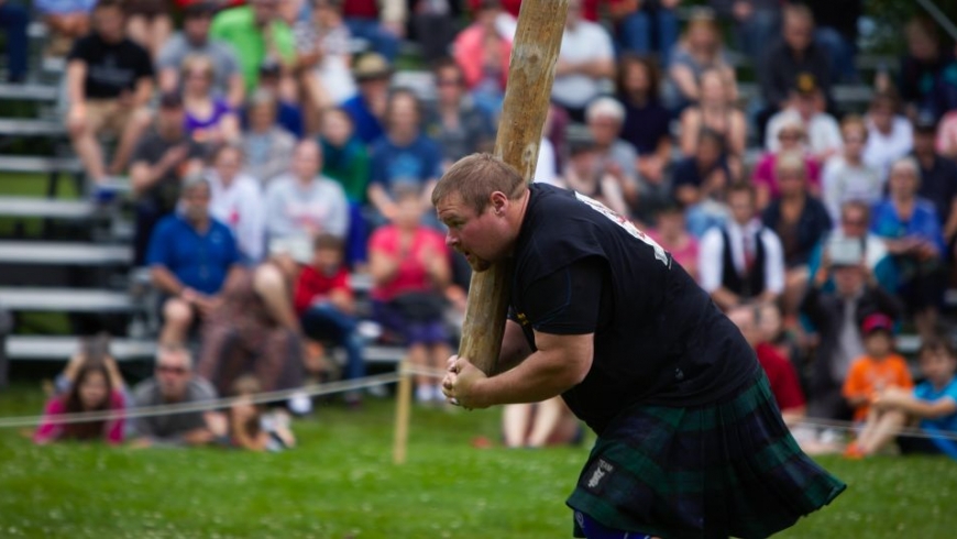 A man in a kilt carrying a log in front of a crowd